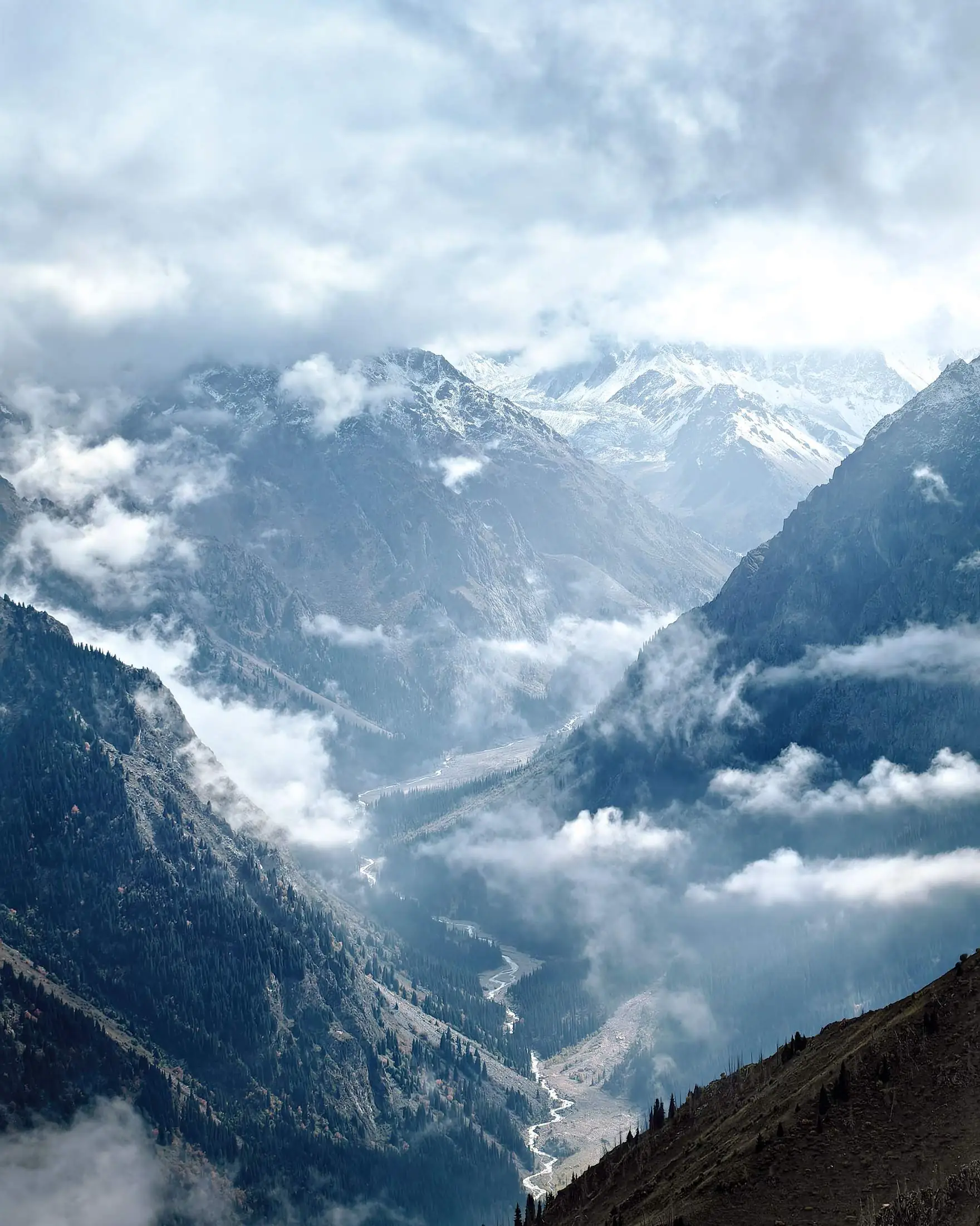 A misty mountain valley with a river winding between snow-capped peaks.